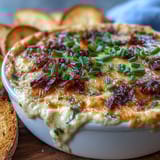 Warm, creamy Smoked Gouda & Onion Dip in a baking dish, garnished with chives and surrounded by crisp vegetables.