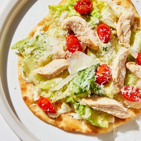 Golden, crisp flatbread topped with sliced grilled chicken, fresh romaine, and creamy Caesar dressing, ready to serve.  