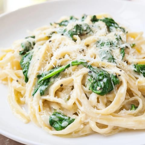 A close-up of Creamy Garlic Spinach Pasta twirled on a fork, revealing tender spinach leaves and melted Parmesan in every savory bite.