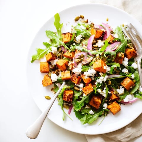 Vibrant roasted sweet potato salad in a white bowl, featuring arugula, red onion, and feta drizzled with honey-lime dressing.