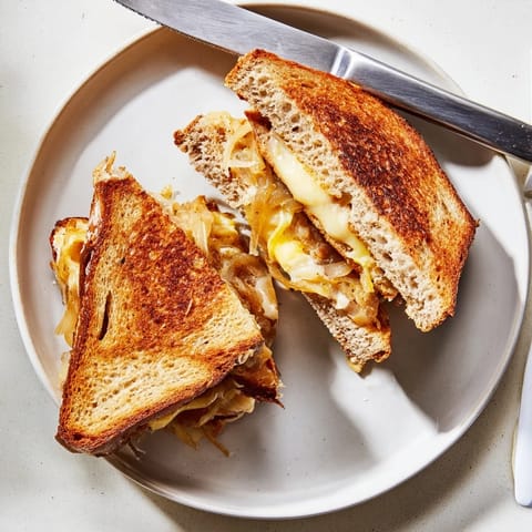 Two golden-brown Caramelized Onion & Gruyère Grilled Cheese sandwiches on rustic country bread.
