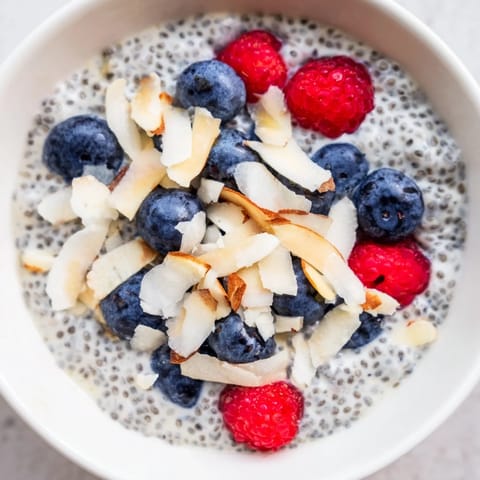 Poppy Seed Chia Pudding layered in a glass jar, garnished with shredded coconut and raspberries.