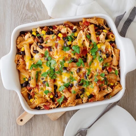 A close-up of Chicken Burrito Pasta Bake, melted cheddar and Monterey Jack cheese bubbling over a layer of black beans and shredded chicken.
