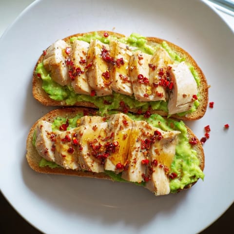 A close-up view of Smashed Avocado Chicken Toast, highlighting juicy grilled chicken slices and crusty sourdough with a honey drizzle.  