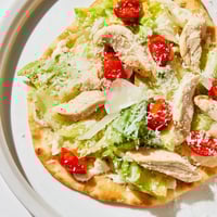 Golden, crisp flatbread topped with sliced grilled chicken, fresh romaine, and creamy Caesar dressing, ready to serve.  