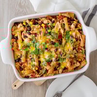 A close-up of Chicken Burrito Pasta Bake, melted cheddar and Monterey Jack cheese bubbling over a layer of black beans and shredded chicken.