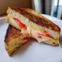 Golden-brown Pepper Jack & Tomato Grilled Cheese slices, melty cheese oozing onto a plate.