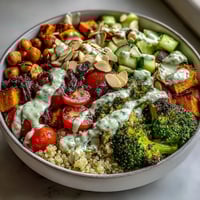 Vibrant meal prep power bowl with quinoa, roasted sweet potatoes, and fresh vegetables topped with crunchy almonds and tahini dressing.  